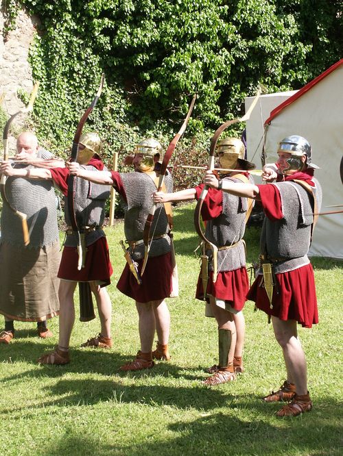 Römische Legionäre in authentischer Kleidung, stehend in Reihe mit gespannten Bögen, bereit, Pfeile abzuschießen.