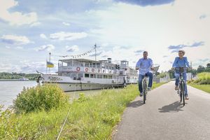 Paar fährt mit Fahrrädern an das Schiff "MS Stadt Wien" an der Tullner Donaulände vorbei