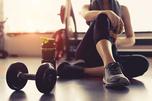 Frau sitzt mit Fitness Hantel und Trinkflasche am Boden 