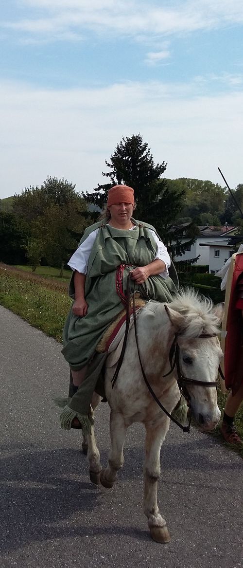 römische Dame auf einem weißen Pferd, gekleidet in antike Roben, während sie majestätisch reitet.