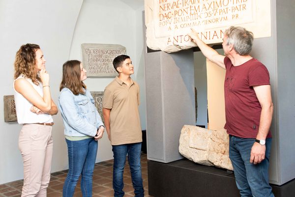 Stadtmuseum Tulln: Ein sachkundiger Mann führt drei Besucher und deutet auf eine römische Tafel.