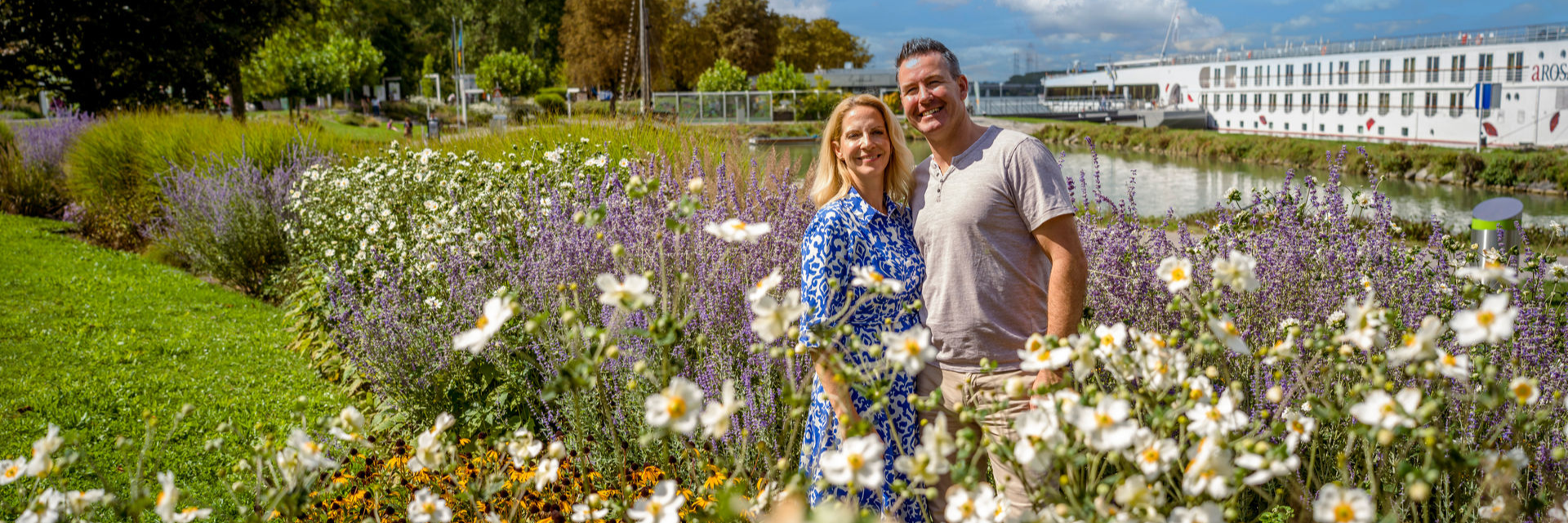 Paar in einem blühenden Garten mit Fluss und Flusskreuzfahrtschiff im Hintergrund