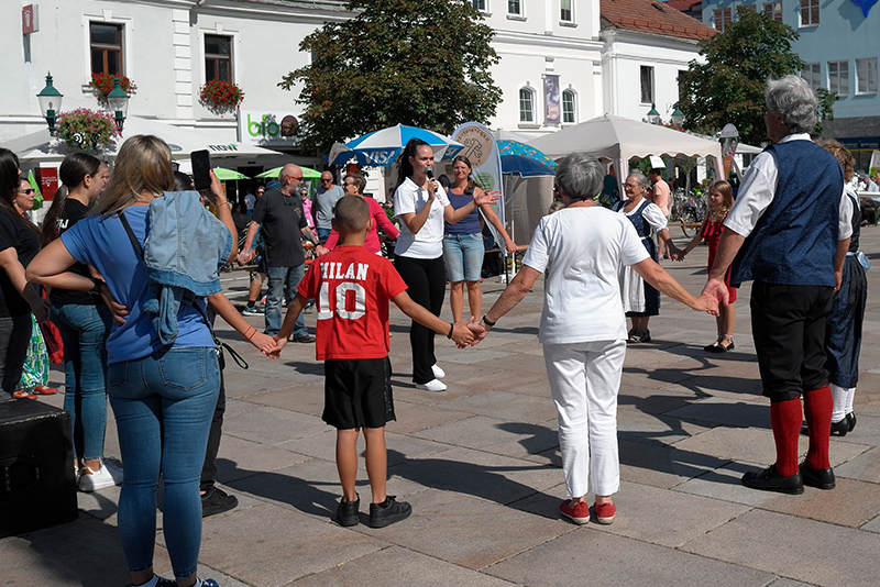 Volksfest: Menschen halten Händchen im Kreis, eine Frau mit Mikrofon leitet an